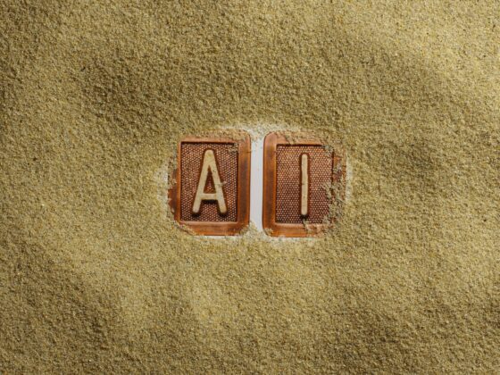 Two clay letter tiles, A and I, partially buried in golden sand on a beach surfacecreme.