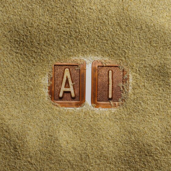 Two clay letter tiles, A and I, partially buried in golden sand on a beach surfacecreme.
