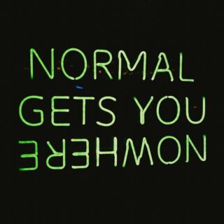 Neon green uppercase sign spelling out words (appears to read) 'NORMAL GETS YOU EMPOWERMENT' against a dark background, viewed from below.