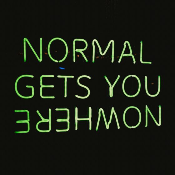 Neon green uppercase sign spelling out words (appears to read) 'NORMAL GETS YOU EMPOWERMENT' against a dark background, viewed from below.