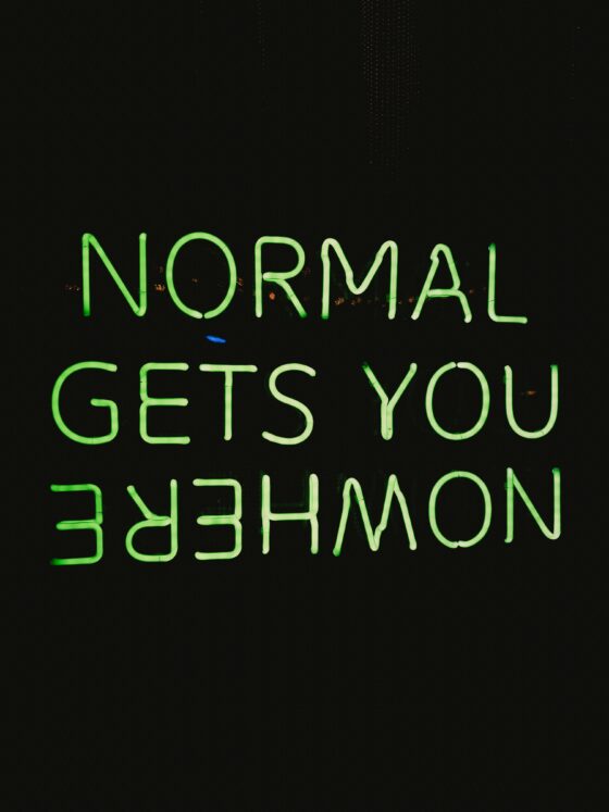Neon green uppercase sign spelling out words (appears to read) 'NORMAL GETS YOU EMPOWERMENT' against a dark background, viewed from below.
