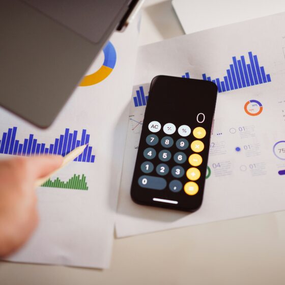 Smartphone and calculator resting on printed financial reports with blue bar charts, charts, and a calendar in the background.
