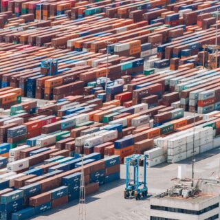 Aerial view of a busy shipping yard with rows of stacked colorful containers and a few trucks nearby