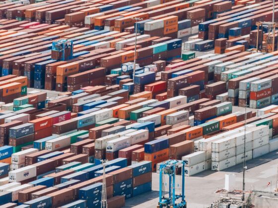 Aerial view of a busy shipping yard with rows of stacked colorful containers and a few trucks nearby