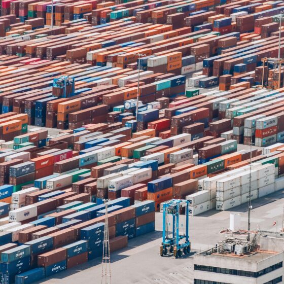 Aerial view of a busy shipping yard with rows of stacked colorful containers and a few trucks nearby