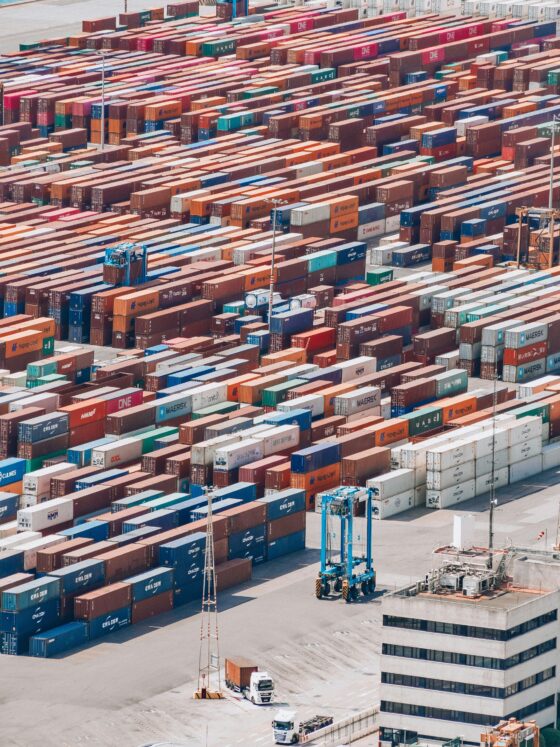 Aerial view of a busy shipping yard with rows of stacked colorful containers and a few trucks nearby