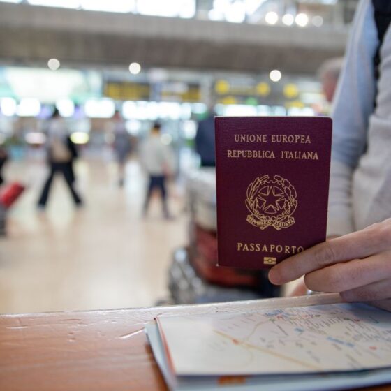 Traveler holding a burgundy Italian passport at an airport counter, with a map on the table in the foreground.