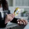Person in a suit uses a laptop with floating holographic hotel management icons, including a reservation system and distribution hub.
