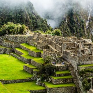 Inca ruins at Machu Picchu with stone terraces and stairways against misty mountains in the background.