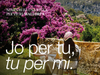 Poster promoting sustainable travel in Mallorca, showing two women seated outdoors with bright pink bougainvillea and mountain backdrop, plus campaign logo and Catalan text.