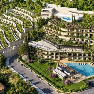 A terraced hillside residential complex with multiple levels, landscaped gardens, and two swimming pools seen from above.