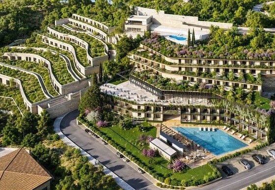 A terraced hillside residential complex with multiple levels, landscaped gardens, and two swimming pools seen from above.