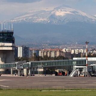 Airport apron with a control tower and jet bridges, city skyline, and snow-capped mountains in the background.