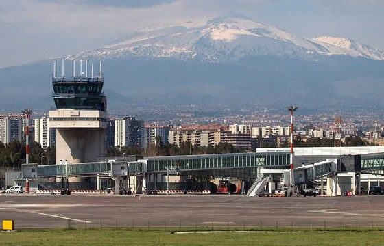 Airport apron with a control tower and jet bridges, city skyline, and snow-capped mountains in the background.