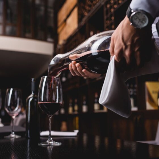 A waiter pours red wine from a bottle into a glass at a bar.