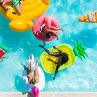 Overhead view of people on colorful pool floats in a bright blue swimming pool on a sunny day the water shimmering around them.