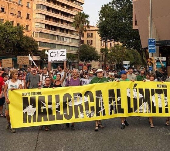 Group of protesters marching down a city street holding a large yellow banner that reads 'Mallorca al dimite!'