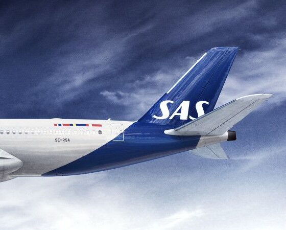 Tail of a SAS commercial jet in blue with white SAS lettering flying against a cloudy blue sky, left fuselage visible.