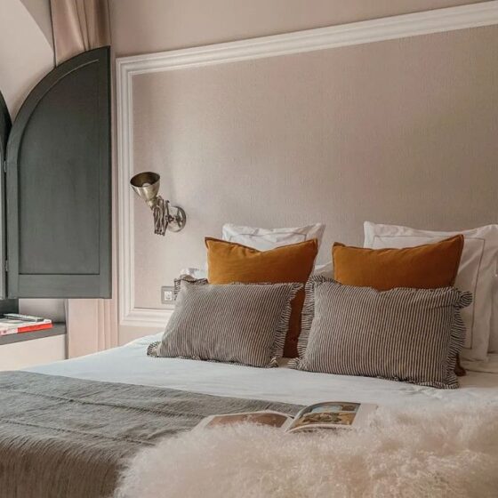 Cozy bedroom with a large arched window, white bedding, a gray throw, and mustard yellow plus striped pillows on the bed.