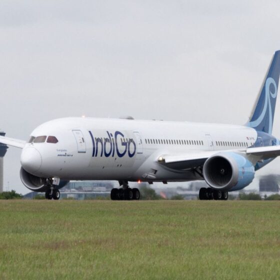 IndiGo airliner taxiing on a runway with a control tower in the background.