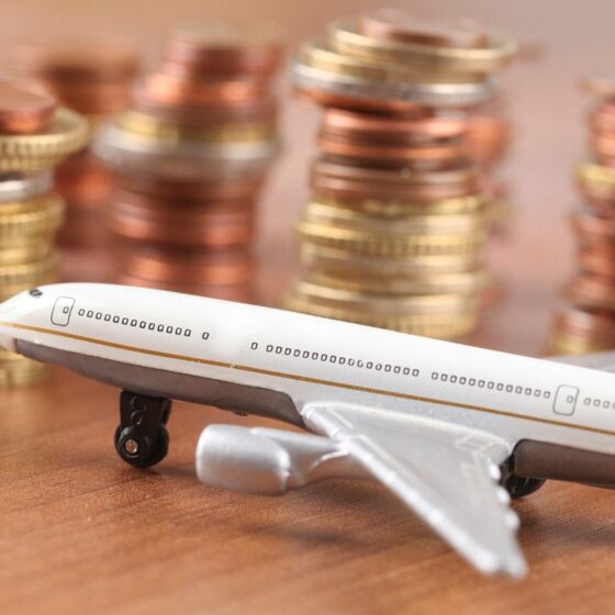 Toy airplane model on a wooden surface with stacks of coins in the background, conveying travel costs or budgeting.