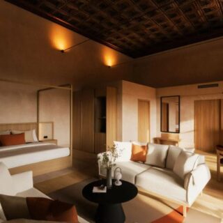 Luxurious hotel suite with a canopy bed, white and orange accents, and a living area under warm lighting.