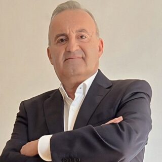 Middle-aged man in a dark suit with arms crossed, looking confidently at the camera.