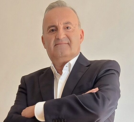 Middle-aged man in a dark suit with arms crossed, looking confidently at the camera.