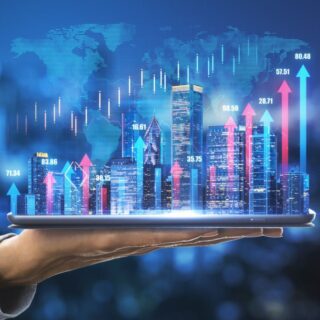 Hand holding a tablet projecting a holographic city skyline with blue and pink arrows and stock data above it (business/finance concept).