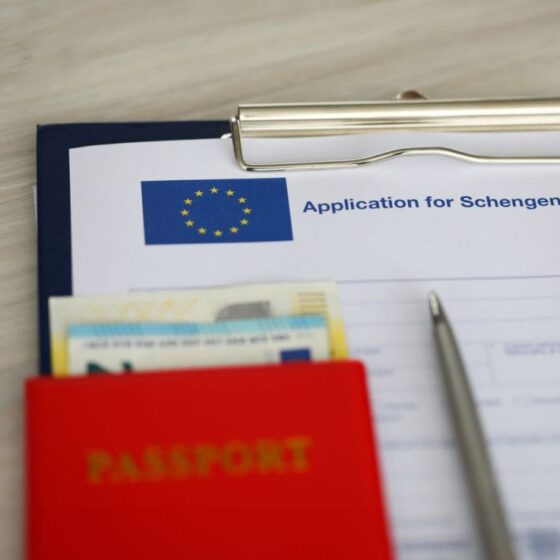 Clipboard with a Schengen visa application form, a red passport case, and a pen on a desk