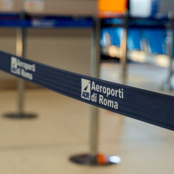 Blue barrier tape in an airport terminal reading 'Aeroporti di Roma' (ADR).