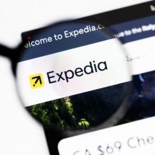 Expedia logo on a computer screen viewed through a magnifying glass, highlighting the brand name and yellow compass icon.