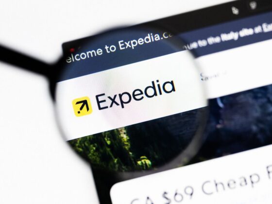 Expedia logo on a computer screen viewed through a magnifying glass, highlighting the brand name and yellow compass icon.