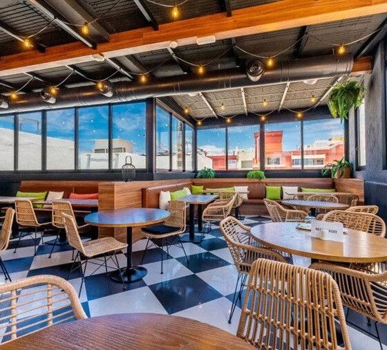 Bright rooftop cafe with wicker chairs, round wooden tables, string lights, and a checkered floor.