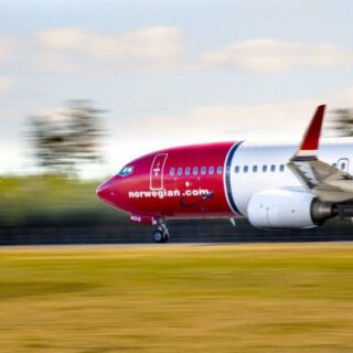 Red Norwegian Air jet taxiing on the runway with a blurred background, branding visible on the nose.