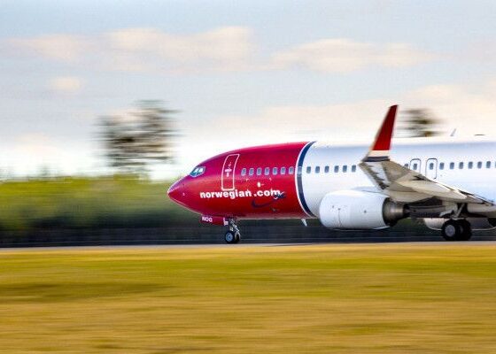 Red Norwegian Air jet taxiing on the runway with a blurred background, branding visible on the nose.