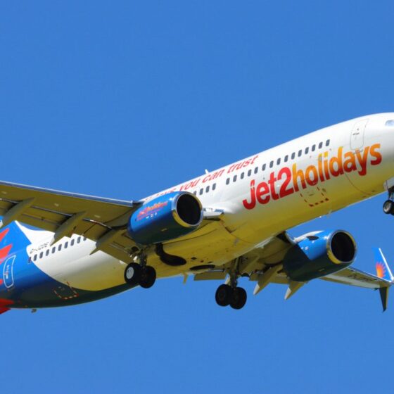 Jet2holidays passenger airplane in clear blue sky, mid-flight, with landing gear retracted and branding visible on fuselage.