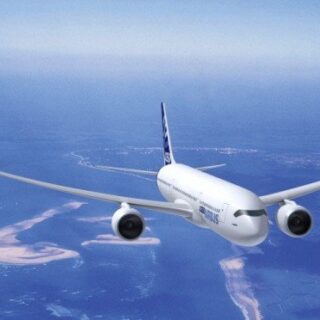 White commercial airliner in flight over a blue ocean and sandy coastline.