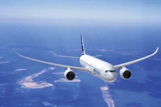 White commercial airliner in flight over a blue ocean and sandy coastline.