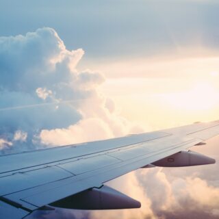 Airplane wing visible from the window with blue sky, fluffy clouds, and warm sunset light.