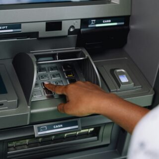 Person entering a PIN on an ATM keypad, with the card slot and receipt area visible above.