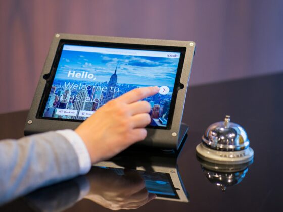 Person taps a tablet-like kiosk showing a city skyline and the words 'Hello, Welcome to Upscale' on the screen.
